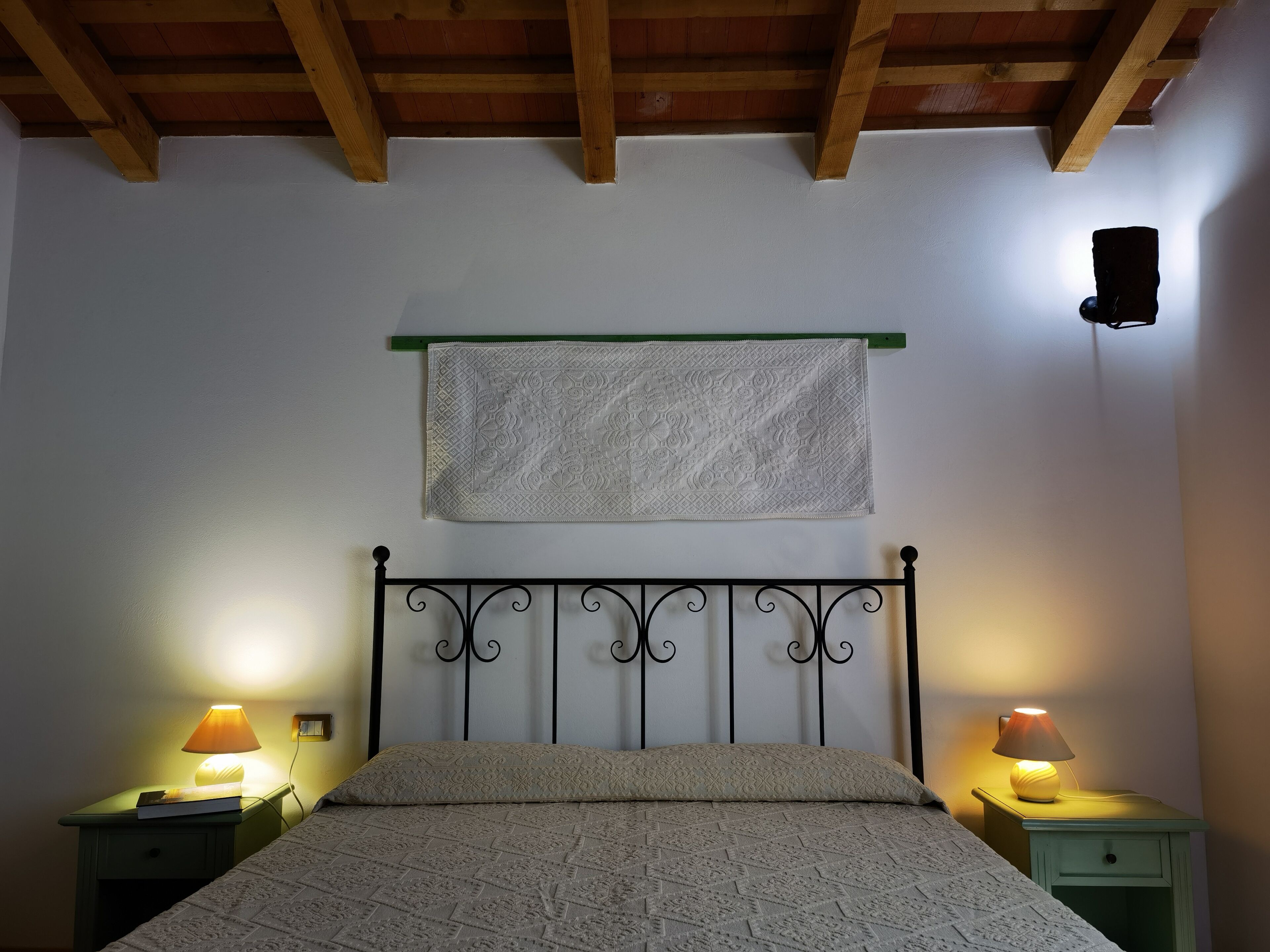 Un dormitorio con una cama, dos mesitas de noche con lámparas, una toalla colgada y un techo de madera.