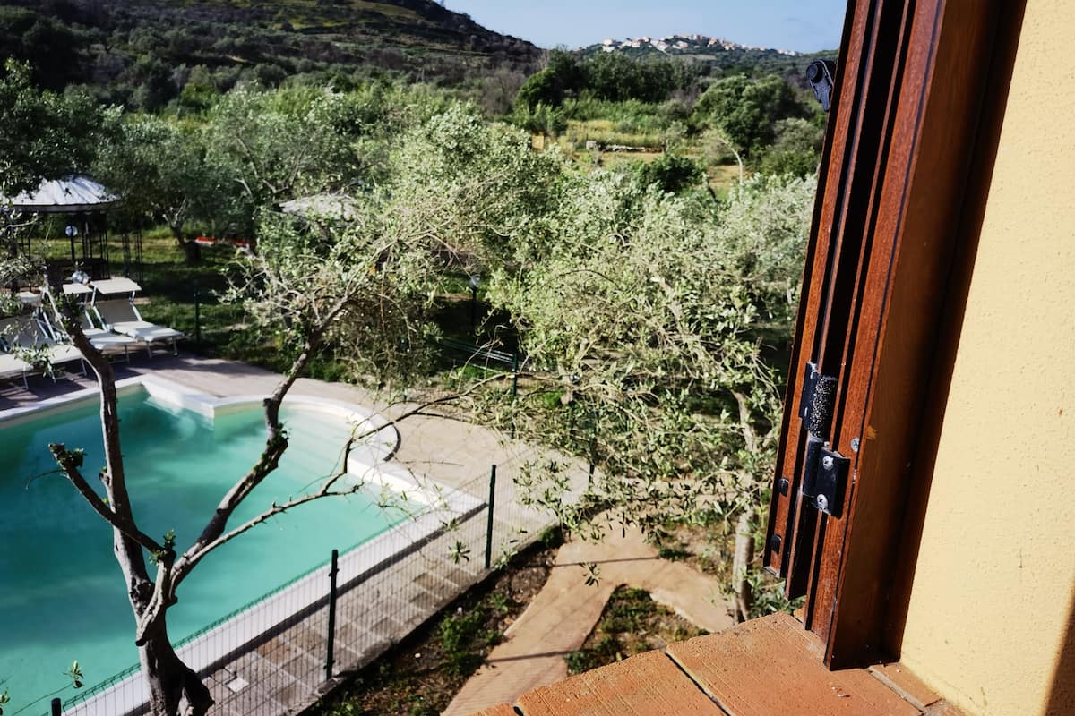 Vista desde un balcón sobre una piscina, con jardín y una colina al fondo.