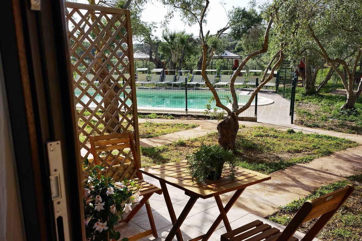 Un patio con una mesa y sillas, una planta en maceta y vistas a una piscina y árboles.