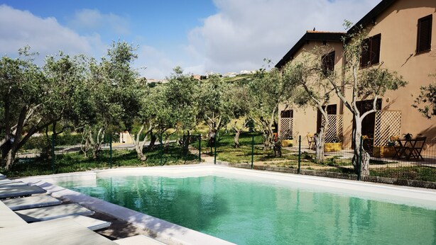 A swimming pool with lounge chairs, surrounded by trees and a building with a sloped roof. - la corte degli ulivi (Tresnuraghes)