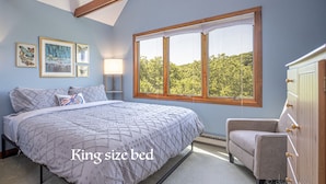 Ein Kingsize-Bett mit gesteppter Auflage, ein Nachttisch mit Lampe, ein Sessel und eine Kommode mit Schubladen.