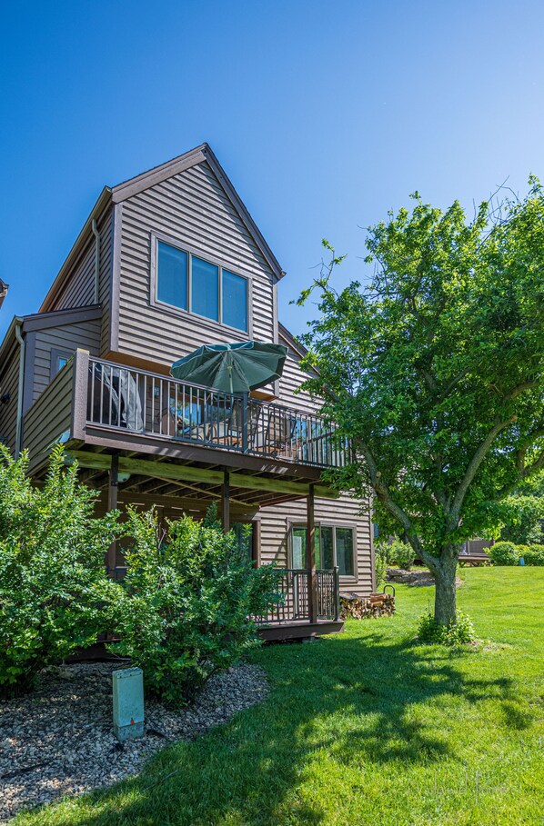 A two-story house with a balcony, a tree, and a grassy yard.