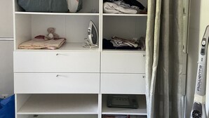 A white storage unit with shelves containing folded blankets, pillows, and a small ironing board. - LE MESNIL, Charming apartment, very well located (Le Blanc-Mesnil)