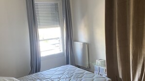 A bedroom with a bed, a window with blinds, a radiator, and a curtain. - LE MESNIL, Charming apartment, very well located (Le Blanc-Mesnil)