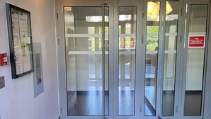 A modern lobby with a glass door entrance, a wall-mounted information board, and a tiled floor. - LE MESNIL, Charming apartment, very well located (Le Blanc-Mesnil)