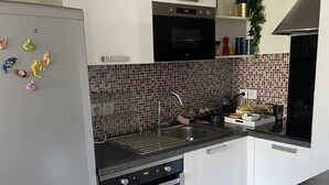A modern kitchen with white cabinets, a black oven, a stainless steel refrigerator, and a tiled backsplash. - LE MESNIL, Charming apartment, very well located (Le Blanc-Mesnil)