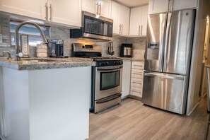 A modern kitchen with stainless steel appliances, white cabinetry, and a granite countertop.