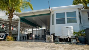 A mobile home with a covered patio area, a water heater, and a palm tree.