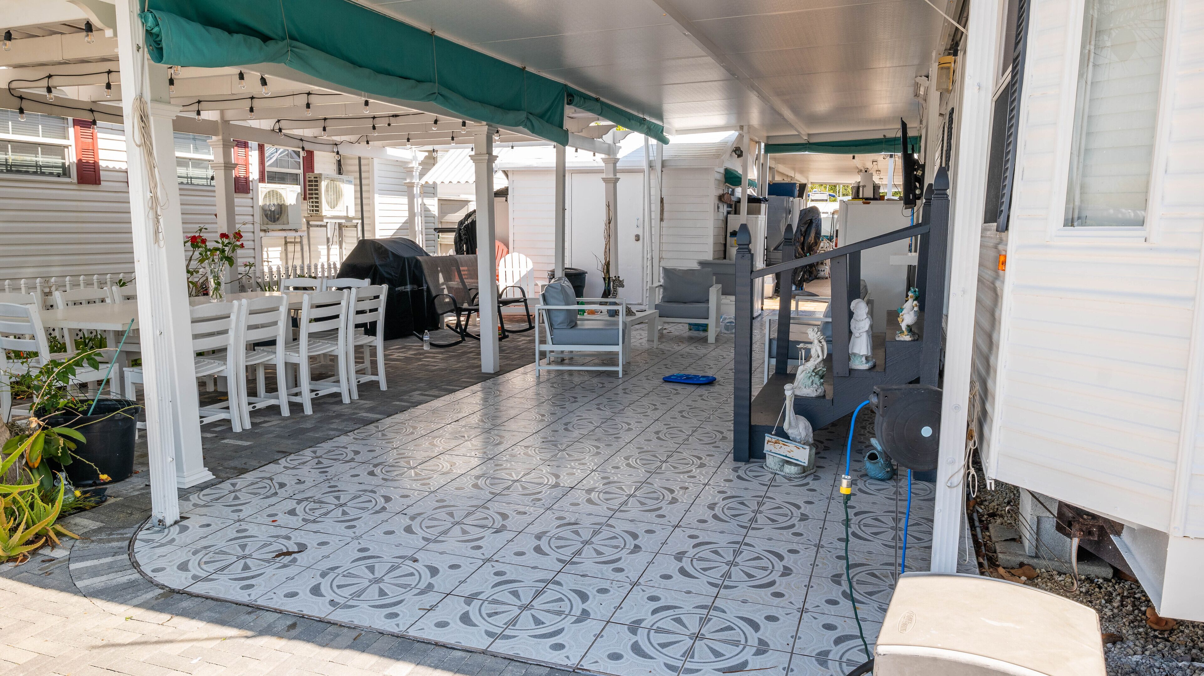 A covered patio area with a patterned floor, white furniture, and a small seating area.
