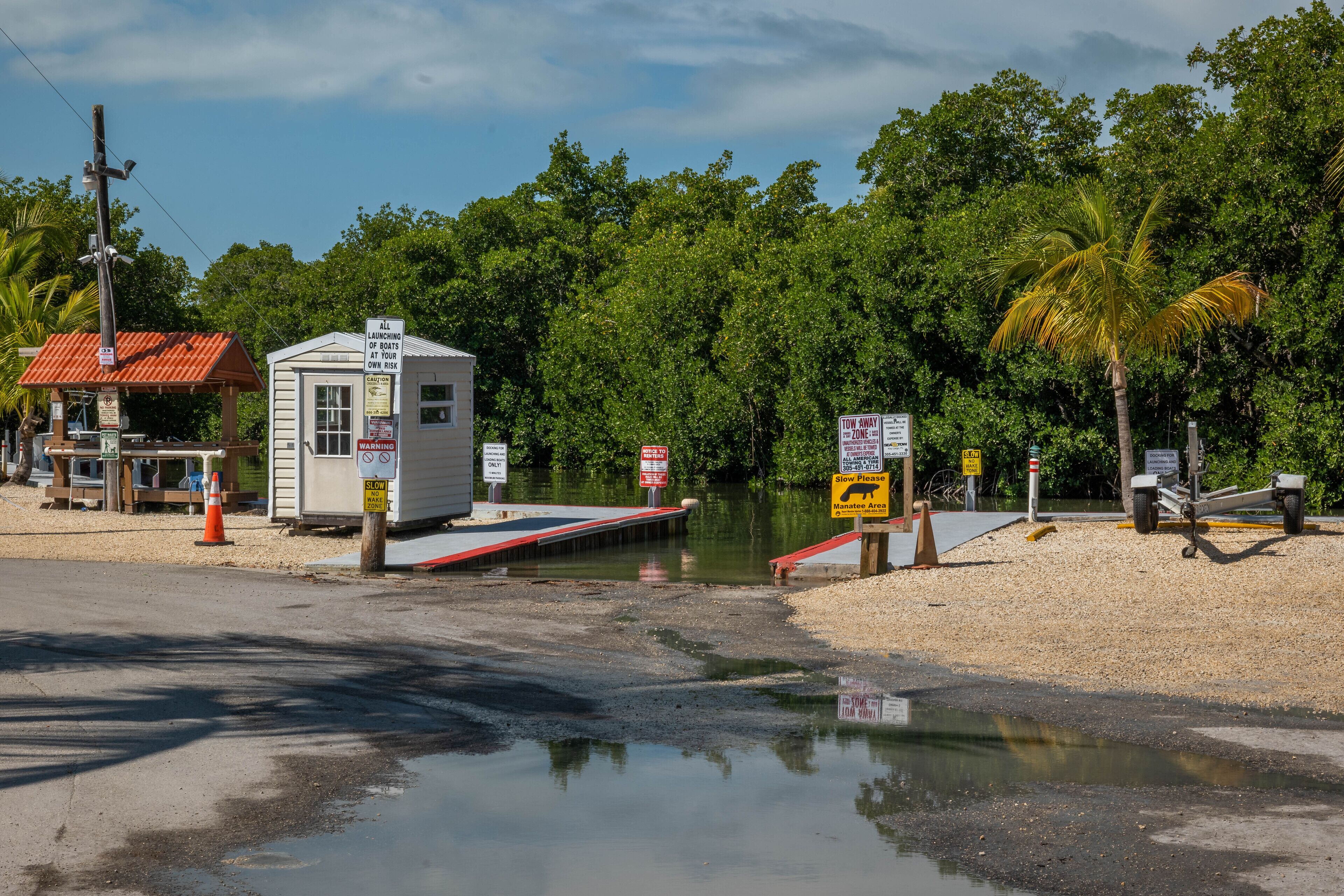 Une zone d’accès à l’eau pour les bateaux, avec un petit bâtiment, des panneaux d’avertissement et un pont enjambant une étendue d’eau.