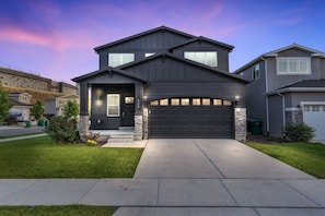 A modern two-story house with a dark exterior, a garage, and a well-maintained lawn.