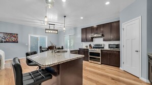 Une cuisine moderne avec des meubles de couleur sombre, un îlot central doté d’un comptoir en granit et des appareils électroménagers en acier inoxydable.