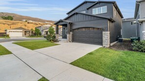 Une maison moderne à deux étages, avec une façade de couleur gris foncé, un garage et une pelouse bien entretenue.