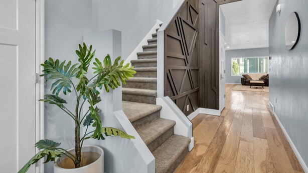 Un escalier au design moderne, une plante en pot et une vue sur un espace de vie avec un canapé.