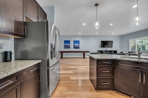 A modern kitchen with dark wood cabinets, granite countertops, a stainless steel refrigerator, and a wooden bench in the center.