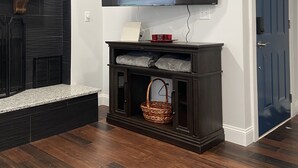 A living room with a flat-screen TV mounted on the wall, a dark wooden cabinet below, and a blue door to the right. - Home Near Main Street-Covered Patio-Hot Tub! (Saint Charles)