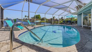 A pool area with a covered patio, lounge chairs, and a clear blue pool.