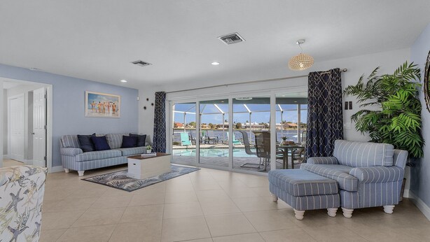 A spacious living room with a large sliding glass door leading to a pool area, a sofa, a coffee table, and a dining area with a view.