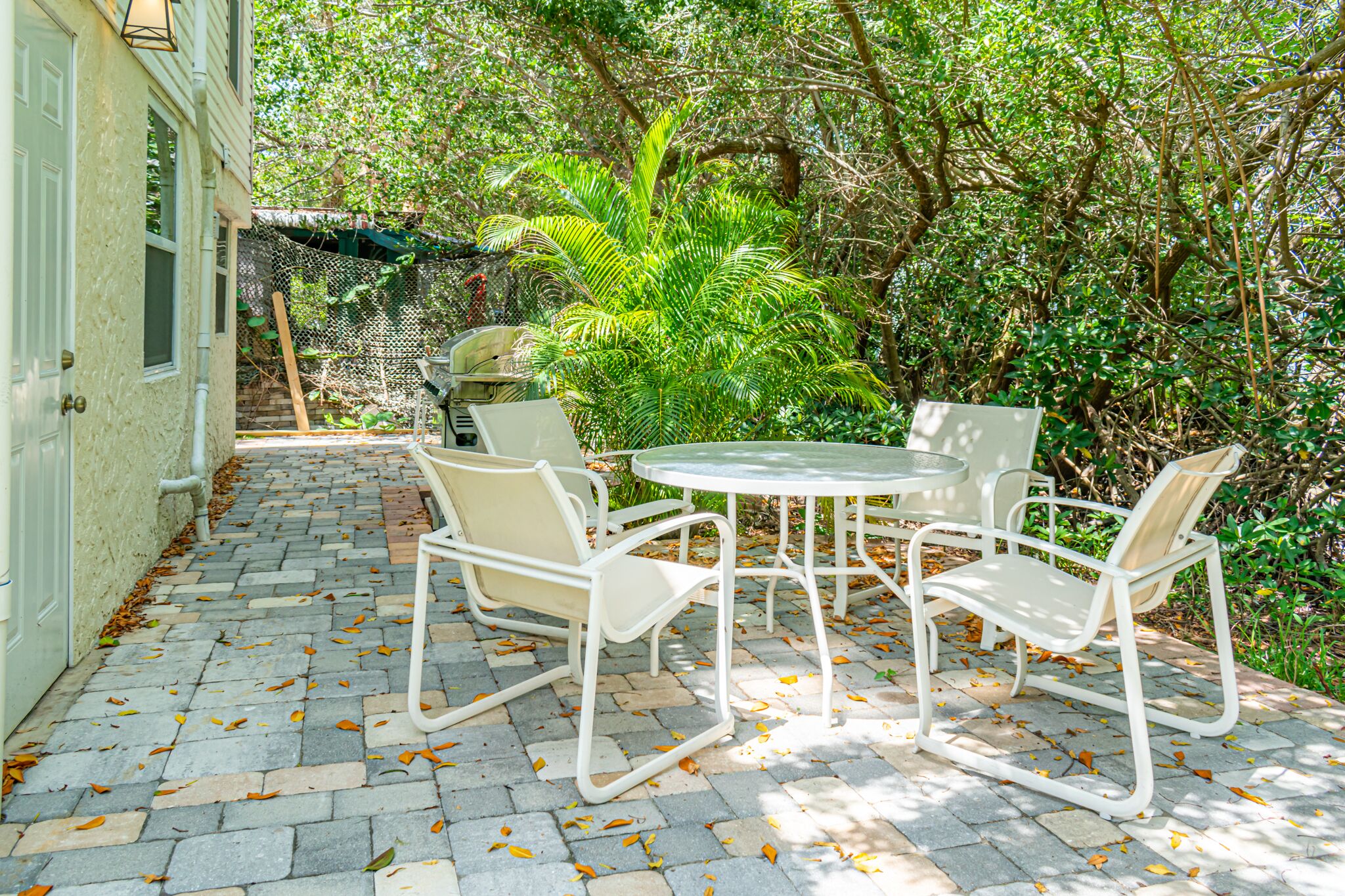Une terrasse avec une table ronde et quatre chaises, entourée d’une zone pavée de pierres et d’une végétation luxuriante.