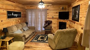 Interior acogedor de una cabaña con detalles de madera, un sofá, un sillón, un televisor y una chimenea.