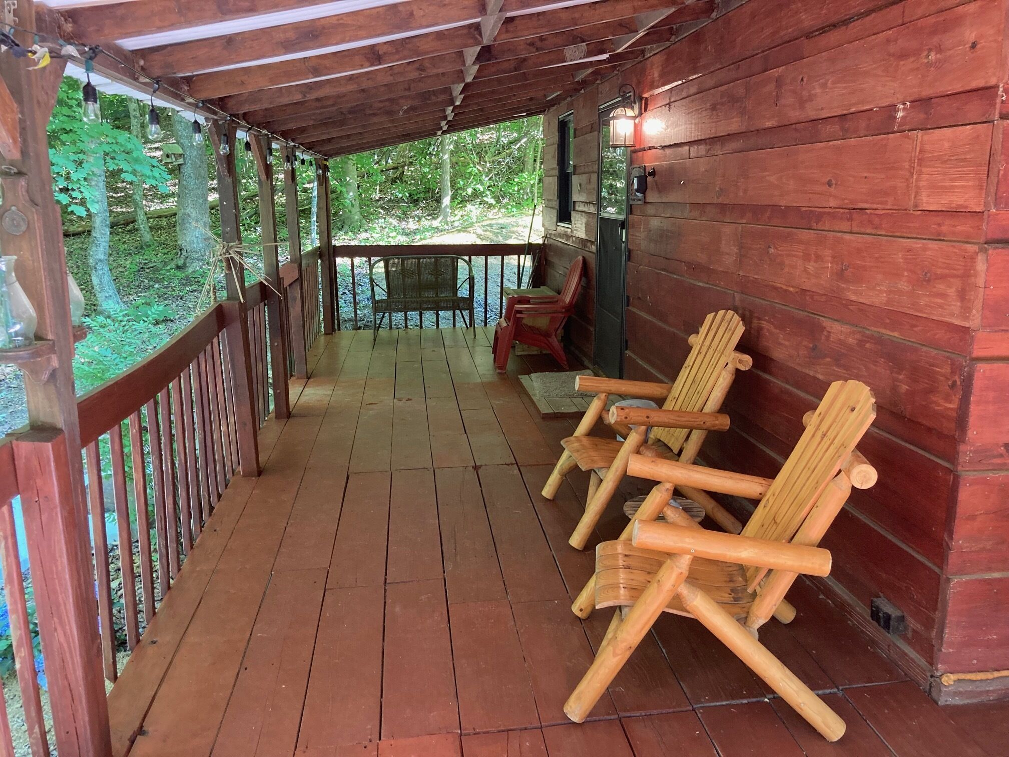 A wooden porch with a railing, a bench, and two Adirondack chairs.