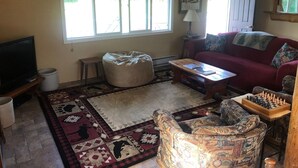 A living room with a TV, a red sofa, a patterned armchair, a coffee table, and a chessboard. - A hunter's/Getaway Paradise (Council)