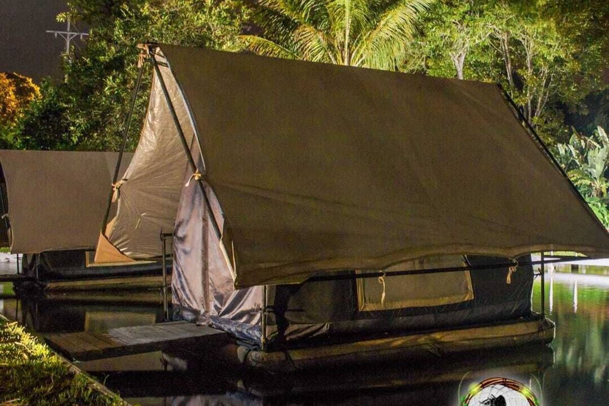 Una estructura cubierta junto a un cuerpo de agua tranquilo, rodeada de abundante vegetación.