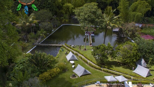 Vista aérea de un complejo turístico con piscina, varias tiendas de campaña y abundante vegetación.