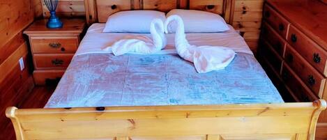 Una cama de madera con colcha azul y dos almohadas con forma de cisne en una habitación tipo cabaña con paredes y suelo de madera.