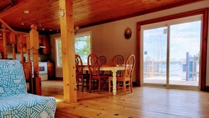 A spacious room with a wooden floor, a dining area with chairs and a table, and a view through a large sliding glass door.