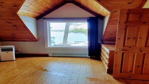 A room with a sloped ceiling, a large window with a view of a lake, a wooden door, and a heater on the floor.