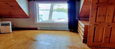 Ett rum med ett sluttande tak, ett stort fönster med utsikt över en sjö, en trädörr och en golvvärmare.