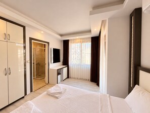 A hotel room with a bed, a desk, a TV, a wardrobe, and a shower. - Livane Sun Otel (Alanya)