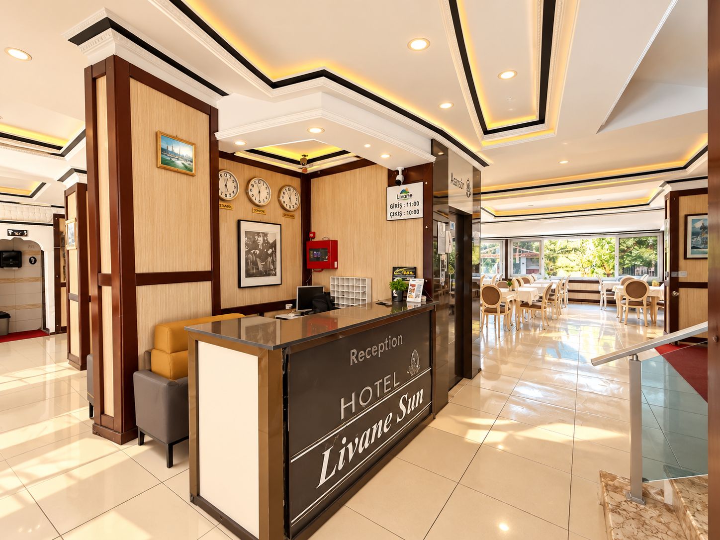 Zona de recepción de hotel con mostrador, relojes y vista al comedor.