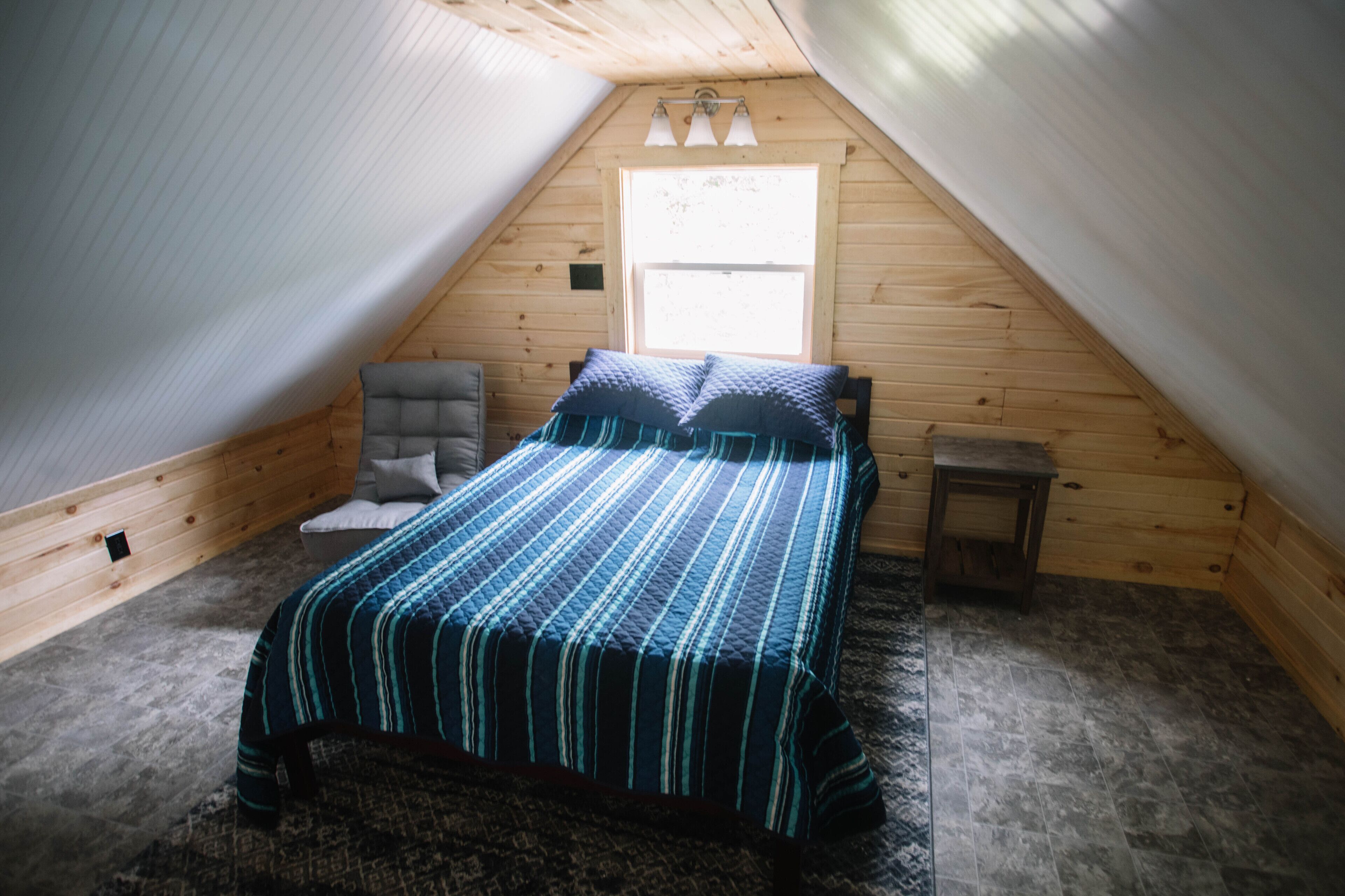 Une chambre à coucher avec un lit, une chaise, une petite table et une fenêtre.