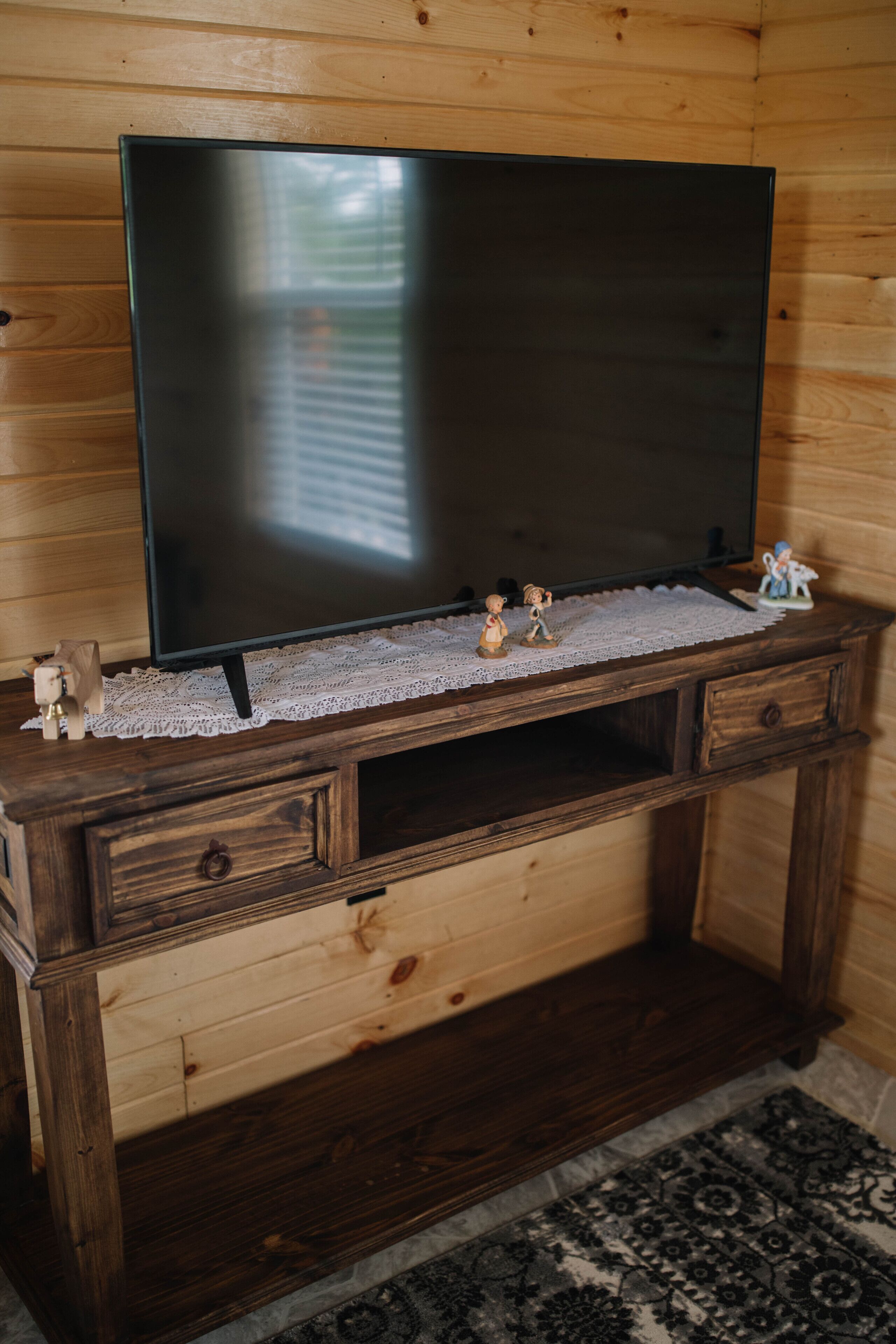 Un mobile in legno contenitore con televisore piatto, un sottile ricamo in pizzo e piccole figurine.