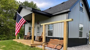 A house with a porch, a swing, and an American flag. - Little House on Dairy- Near Ark- Feed Grain to Calves and Goats (Dry Ridge)