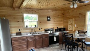 A wooden cabin kitchen with a refrigerator, stove, sink, and dining area. - Little House on Dairy- Near Ark- Feed Grain to Calves and Goats (Dry Ridge)