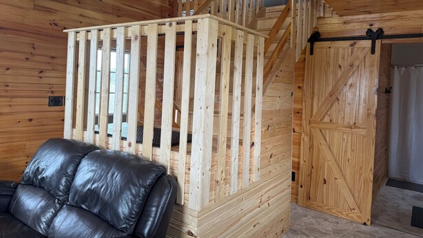 A wooden interior with a staircase, a black leather sofa, and a wooden door. - Little House on Dairy- Near Ark- Feed Grain to Calves and Goats (Dry Ridge)