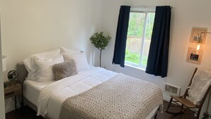 A bedroom with a bed, a nightstand, a chair, a window with curtains, and a wall-mounted light fixture. - Affordable and Spacious unit 1 block from the Seattle Light Rail! (Seattle)