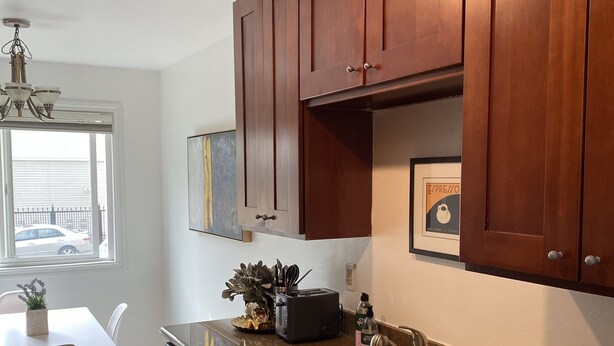 A modern kitchen with dark wooden cabinets, a granite countertop, a double sink, and a dining area with a white table and chairs. - Affordable and Spacious unit 1 block from the Seattle Light Rail! (Seattle)