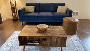 A modern living room with a dark blue sofa, a wooden coffee table with a book, a decorative bowl, and a brown ottoman. - Affordable and Spacious unit 1 block from the Seattle Light Rail! (Seattle)
