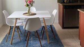 A dining area with a white table, four chairs, a blue rug, and a vase with flowers. - Affordable and Spacious unit 1 block from the Seattle Light Rail! (Seattle)