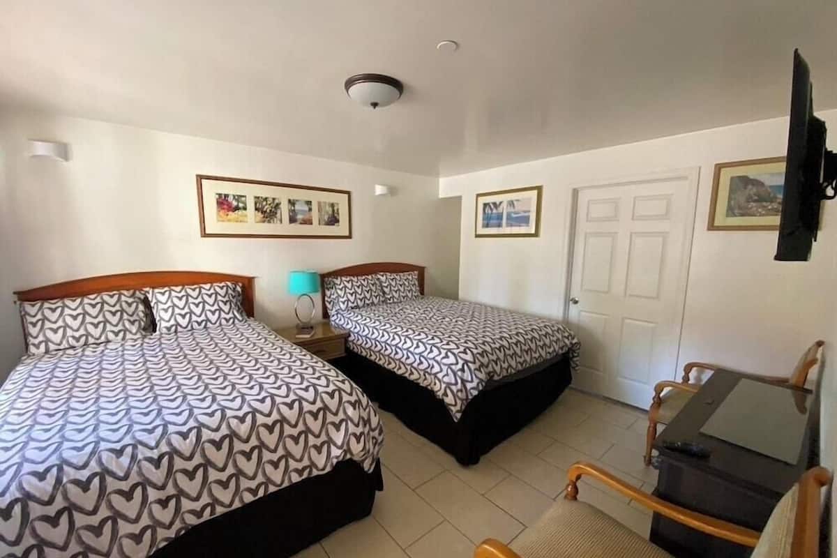 Ein Hotelzimmer mit zwei Betten, einem Schreibtisch, einem Stuhl, einem Fernseher und gerahmten Bildern an den Wänden.