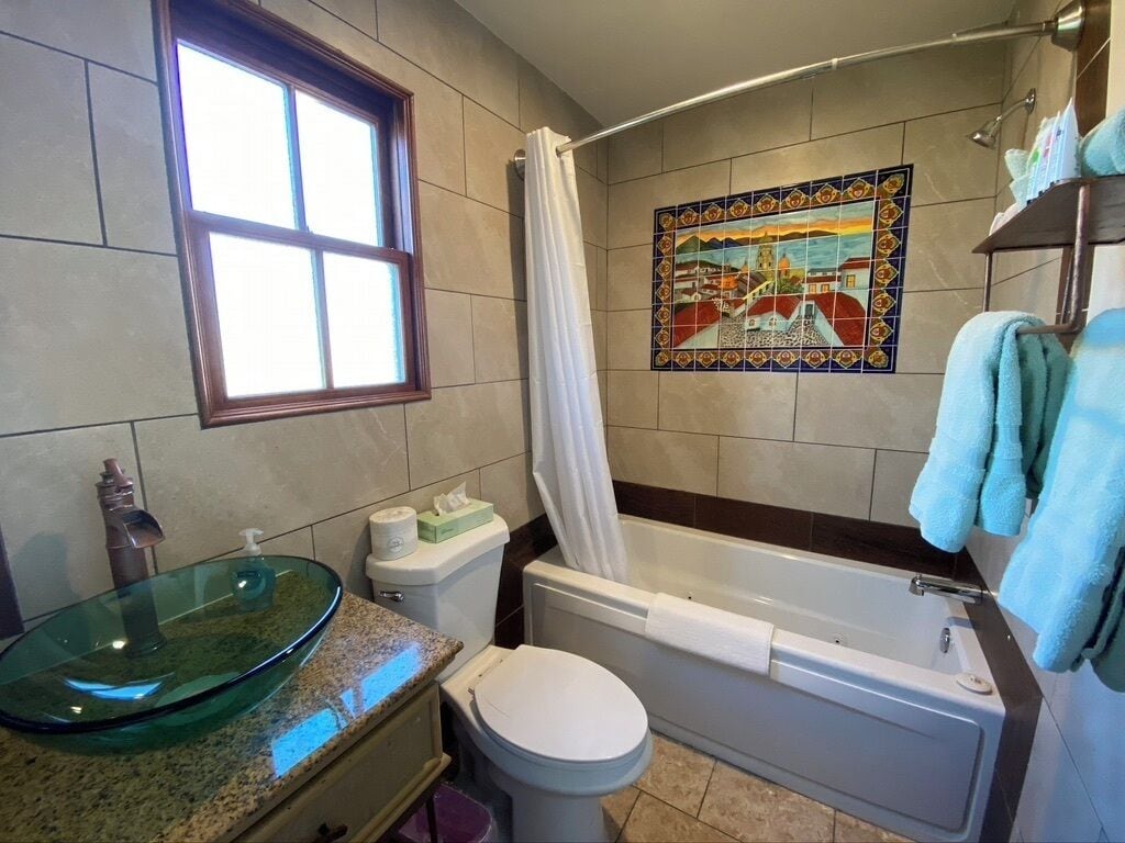 Ein Badezimmer mit einem Glaswaschbecken, Toilette, Badewanne und einer Duschvorhang.
