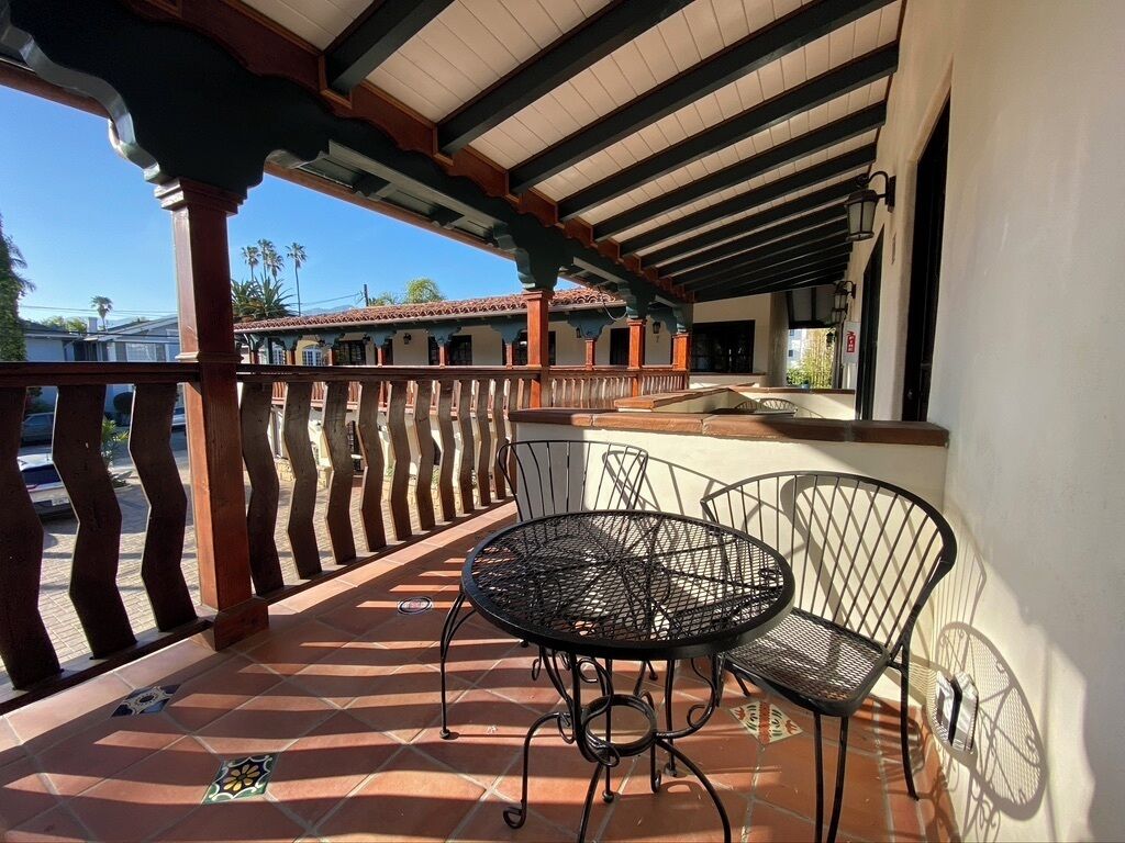 Une terrasse couverte avec une table ronde en métal et deux chaises, un sol carrelé et une rambarde.