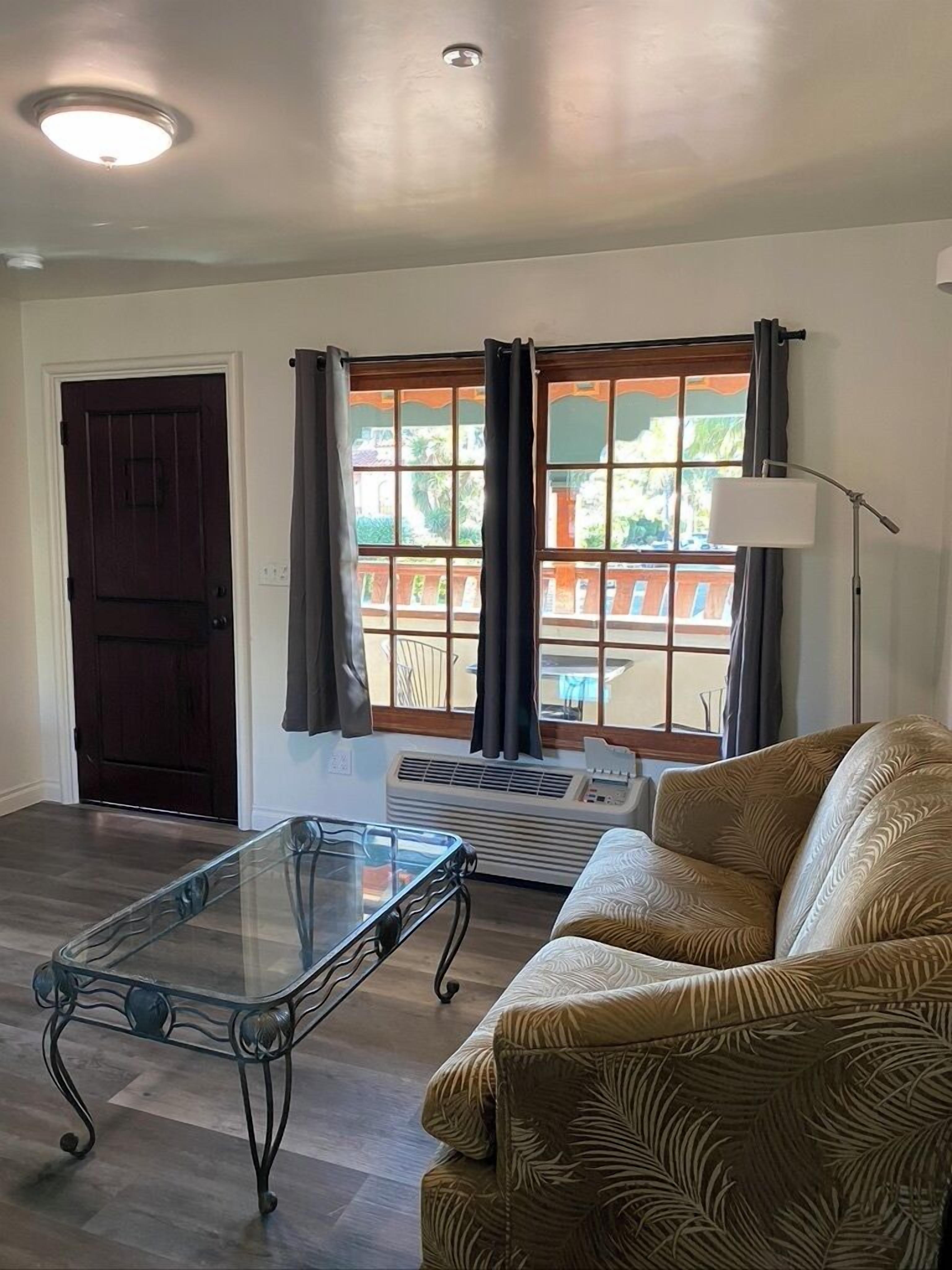 A living room with a glass coffee table, a sofa, a dark door, and a window with curtains.