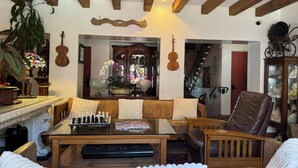 A cozy living room with a wooden ceiling, a glass coffee table, a sofa, a leather armchair, and a chessboard. - Tide Pool Villas (Santa Barbara)