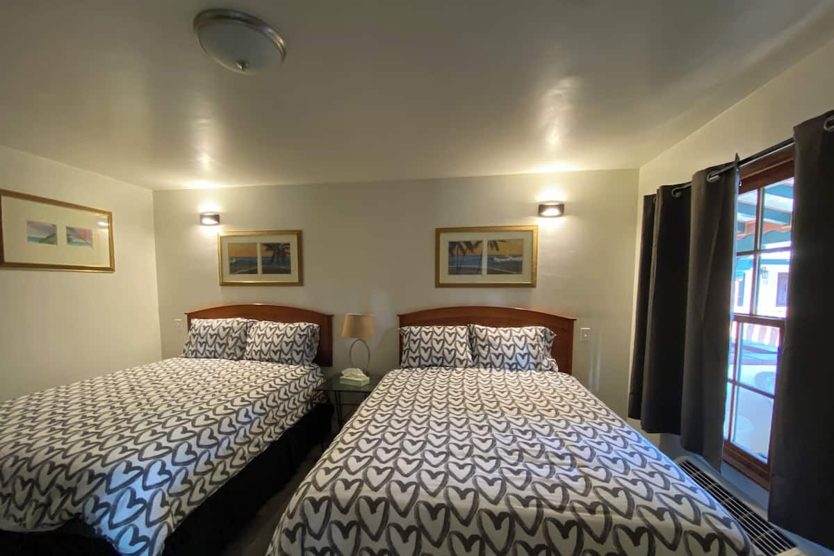 Ein Hotelzimmer mit zwei Betten, jeweils mit gemusterten Bettwäsche, einem Nachttisch mit Lampe und Wandbildern.