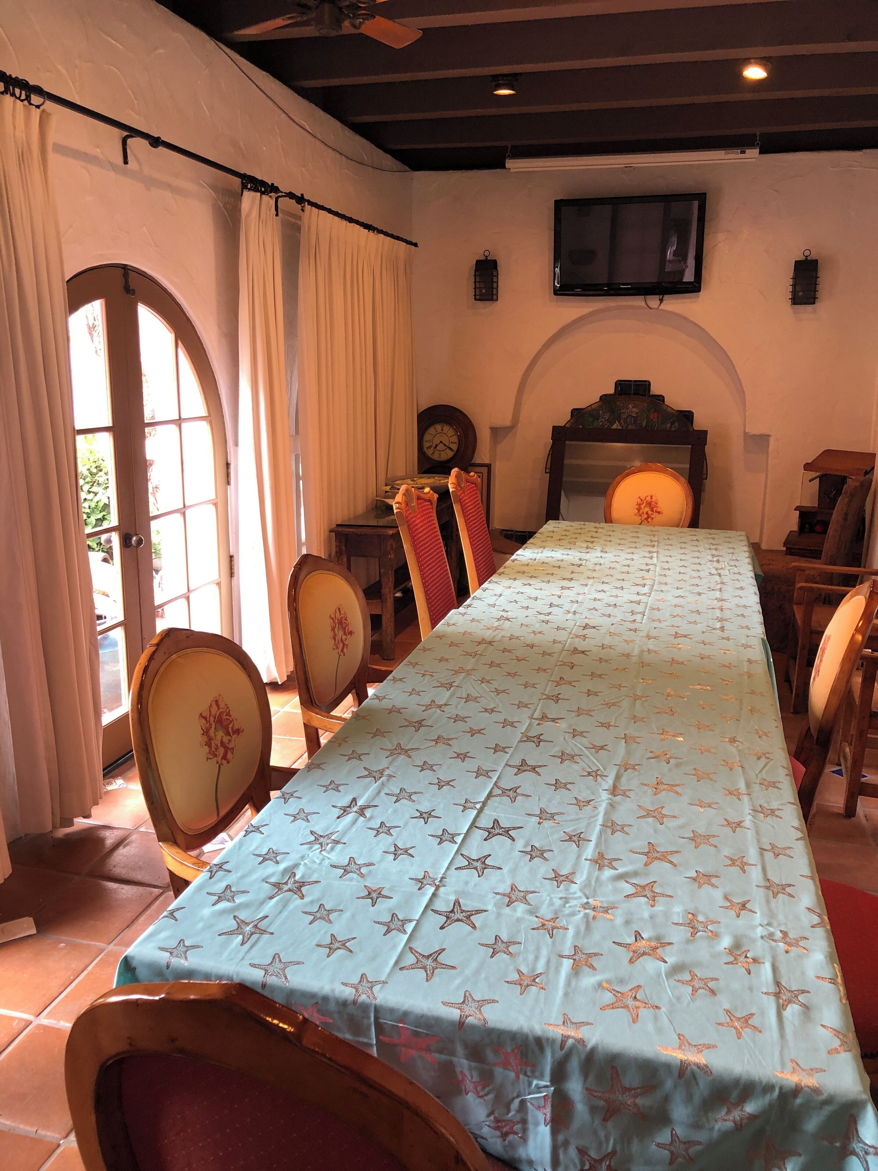 A dining area with a long table covered by a star-patterned tablecloth, surrounded by wooden chairs with floral upholstery.